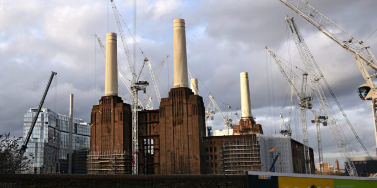 Two chimneys of Battersea Power Station surrounded by multiple cranes. 