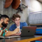 2 students sitting together, looking at a laptop.