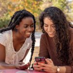 Two students sitting on a table, looking at the screen of one phone.