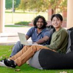 Two students from culturally diverse backgrounds sit together with a laptop
