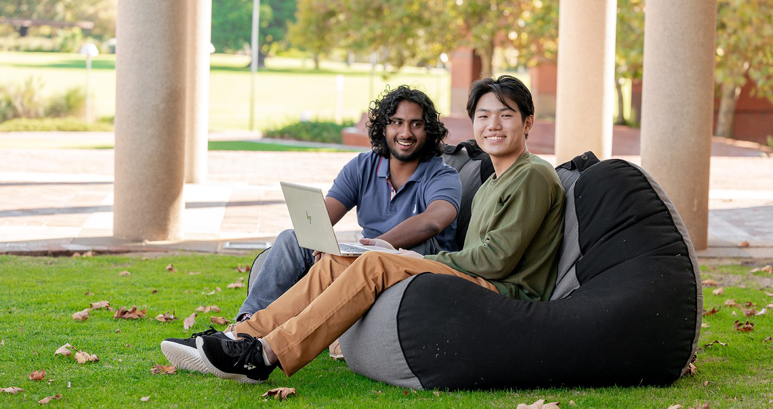 Two students from culturally diverse backgrounds sit together with a laptop