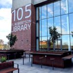 Level 4 outdoor terrace. Wooden benches, some trees and the TL Robertson Library sign is visible on the side of the building.