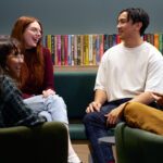 Three students sitting in the Library talking to each other.