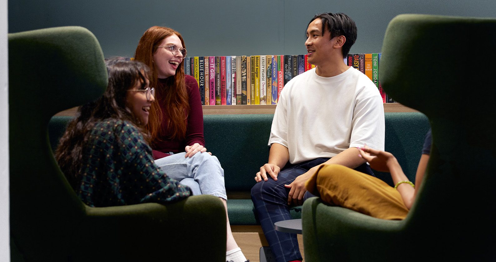 Three students sitting in the Library talking to each other.