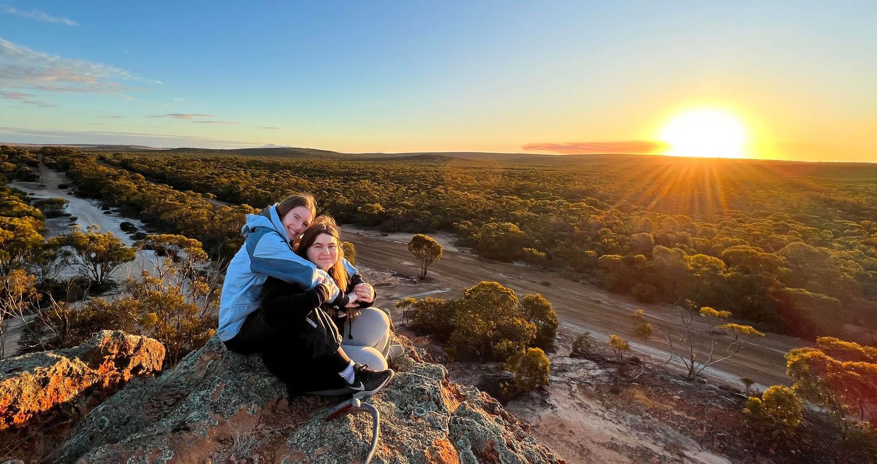Two students embracing while the sun rises.