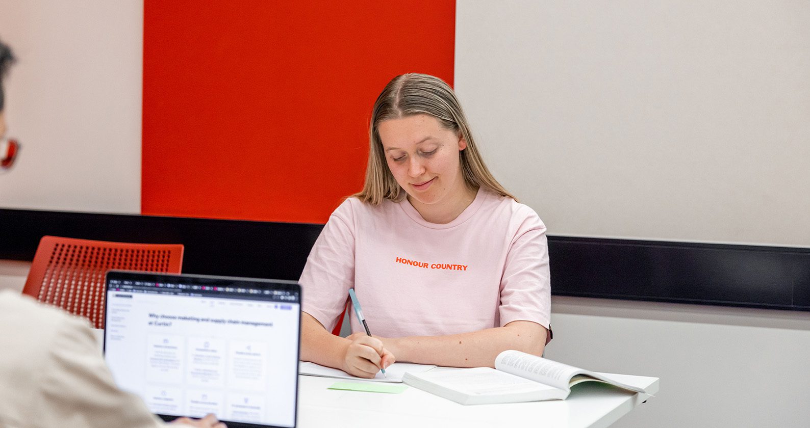 A student writes in her notebook with a textbook open.