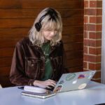 A female student wearing headphones and look at and typing on a laptop.