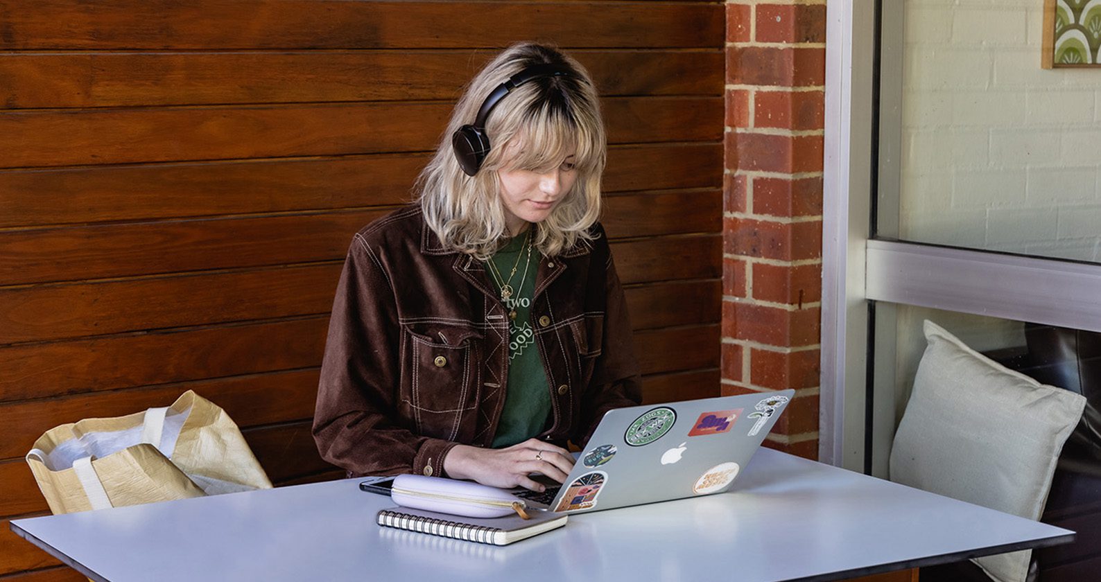 A female student wearing headphones and look at and typing on a laptop.