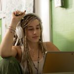 A student with headphones observing something on her laptop.