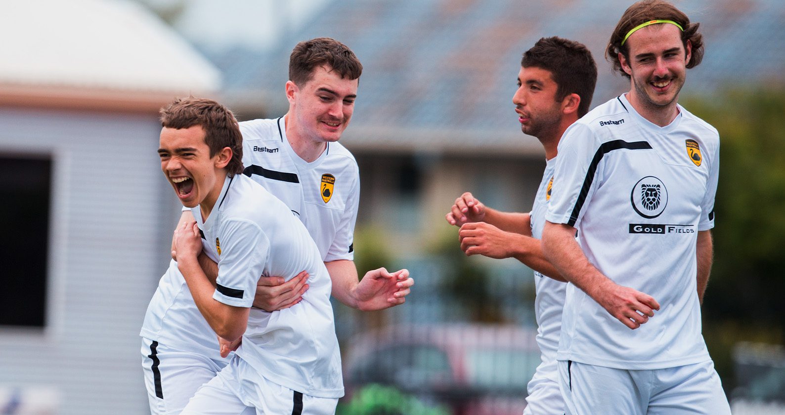 Four athletes wearing white t-shirts playing football.