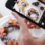 Hands holding a smartphone taking a photo of fruit on a plate.