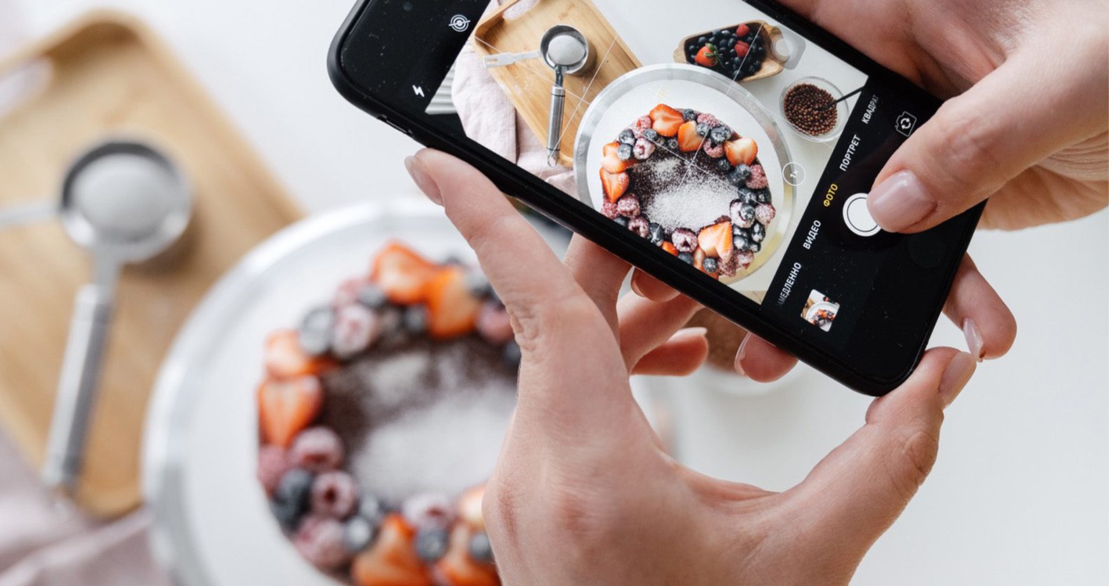 Hands holding a smartphone taking a photo of fruit on a plate.
