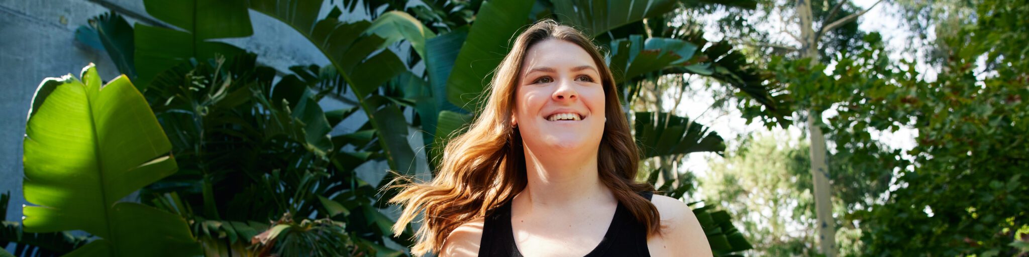 Student smiling on campus walking through the trees with their hair blowing through the wind