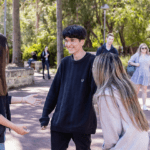Three students standing outdoors talking to each other.