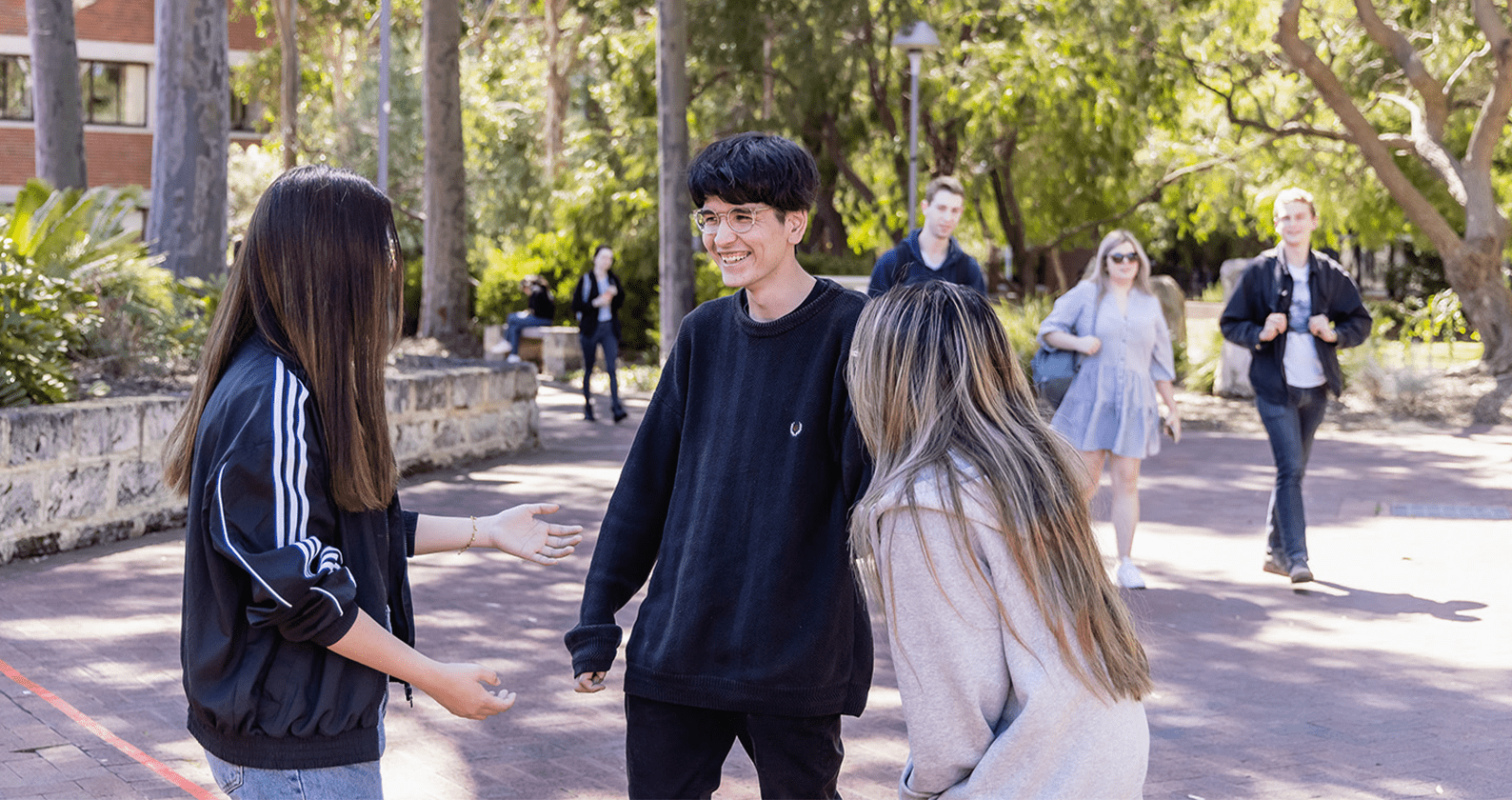 Three students standing outdoors talking to each other.