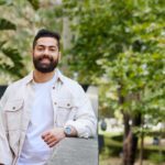 Student wearing a white button up shirt, leaning on a wall