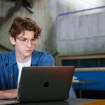 Student sitting indoors looking at a grey laptop.