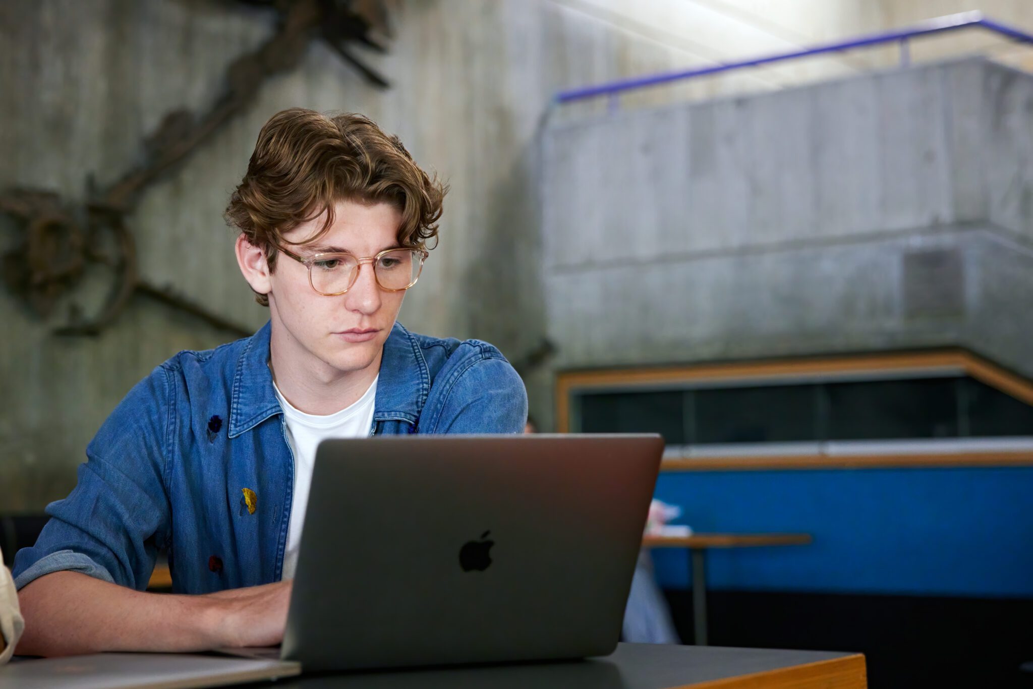 Student sitting indoors looking at a grey laptop.