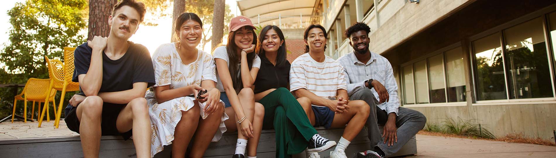 A diverse group of male and female students sitting outside a Curtin building at Bentley Campus.
