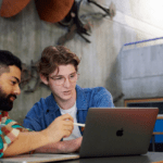 Two students looking at a grey laptop.