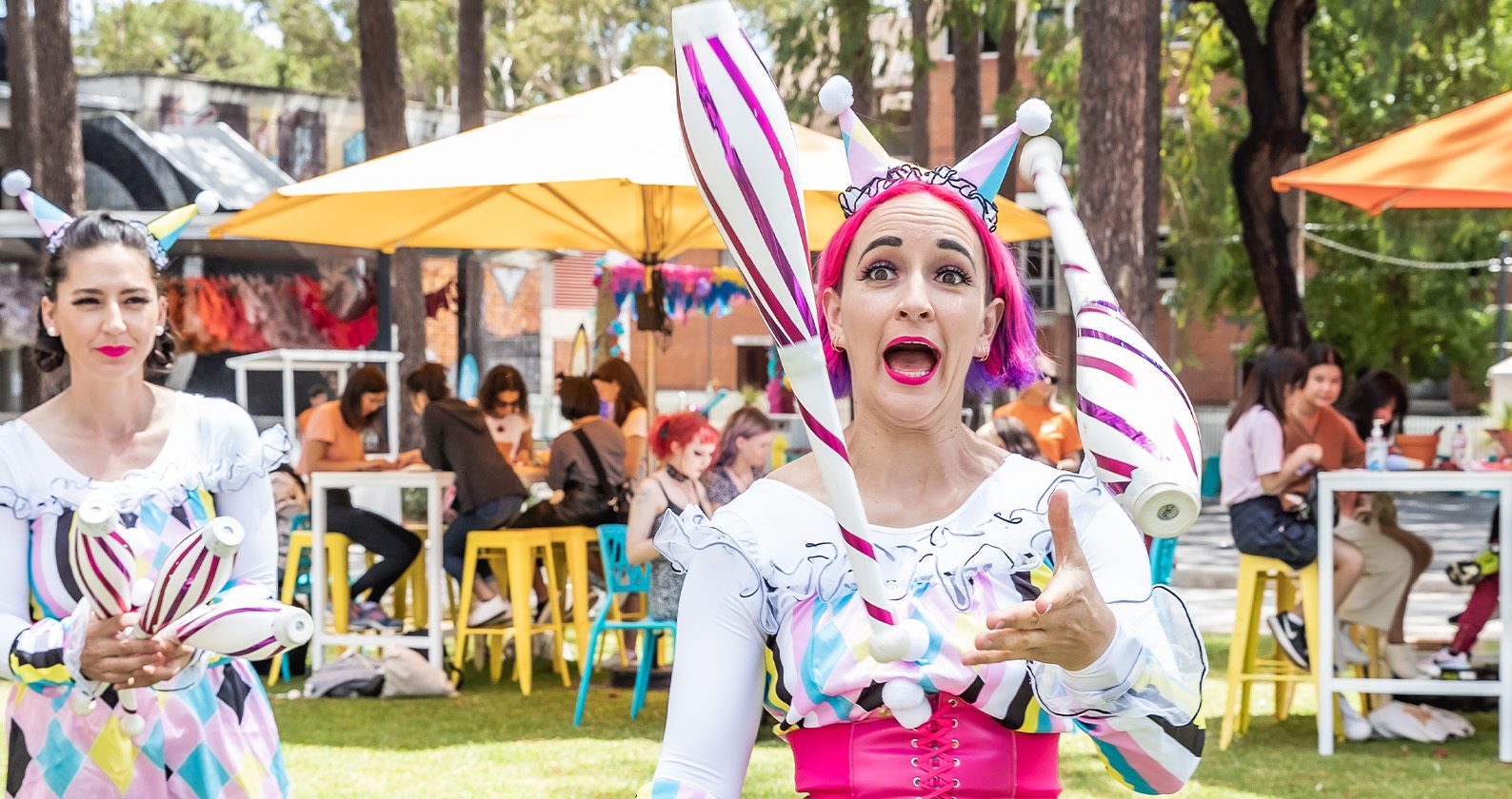 A street performer juggles bowling pins while another performer watches.