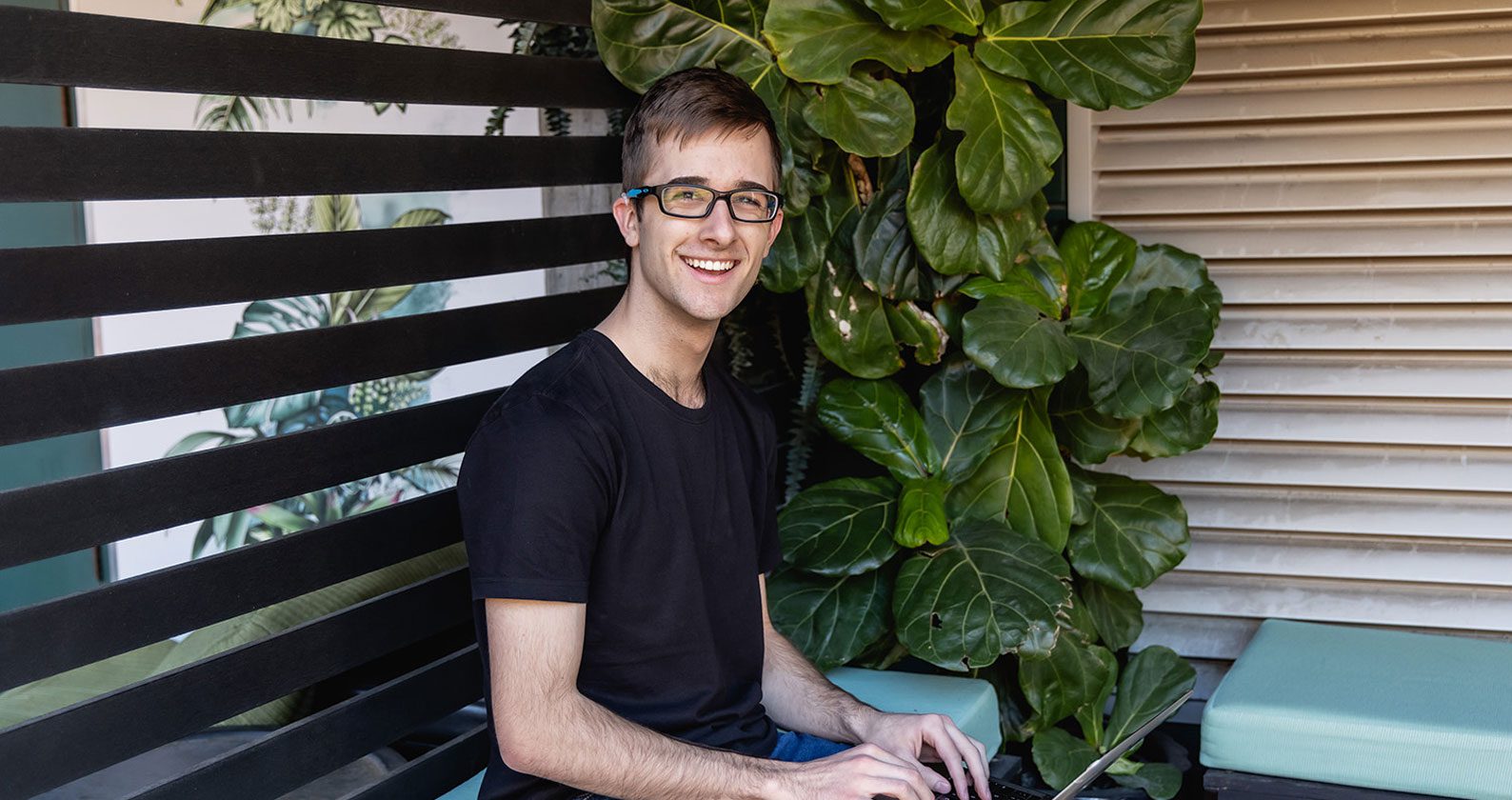 A student is sitting on a bench with his laptop.