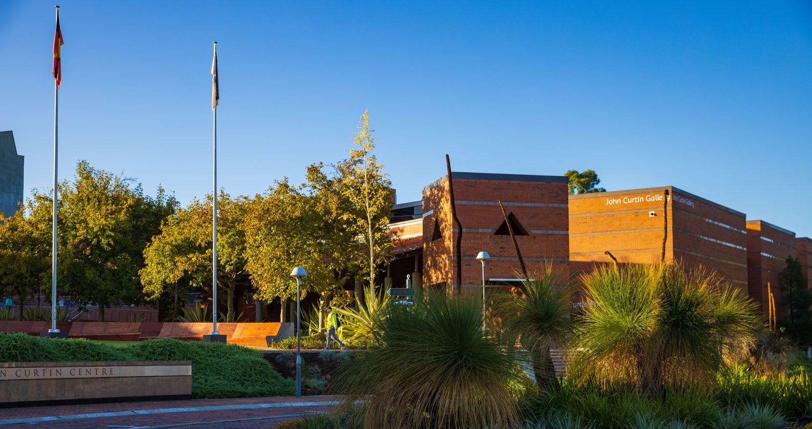 A blue sky over a building and the flagpoles on the Curtin Perth campus.