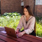A female student sitting at an outdoor table and working on a laptop
