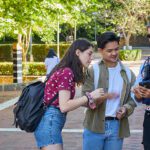 A male and female student speaking with a male Safer Community team member who is showing the students something on a phone.