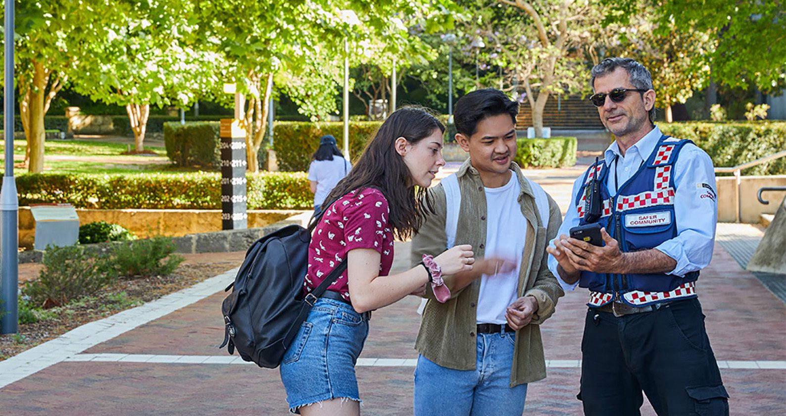 A male and female student speaking with a male Safer Community team member who is showing the students something on a phone.