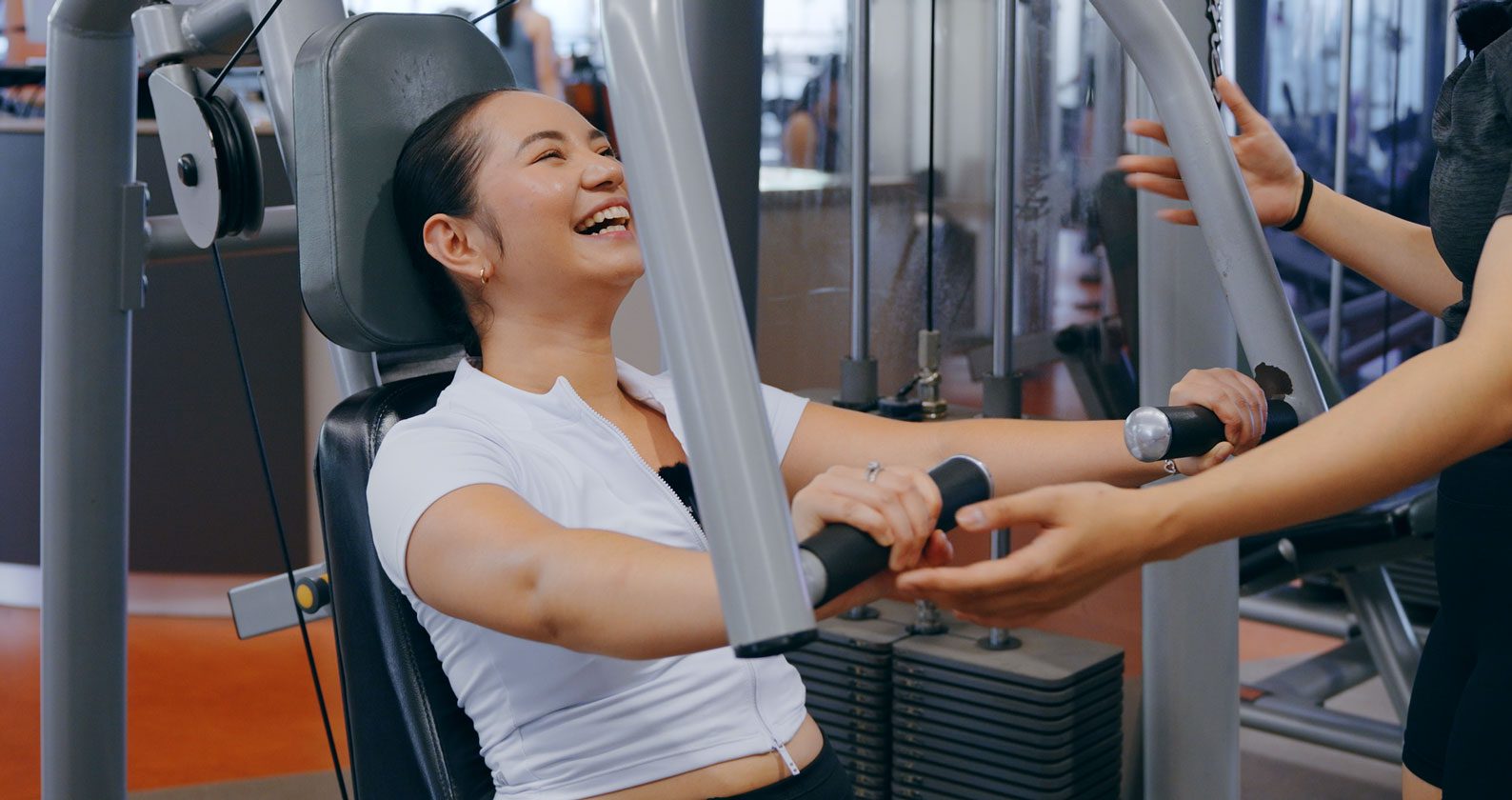 Celena is laughing while on a gym machine. She wears workout gear.