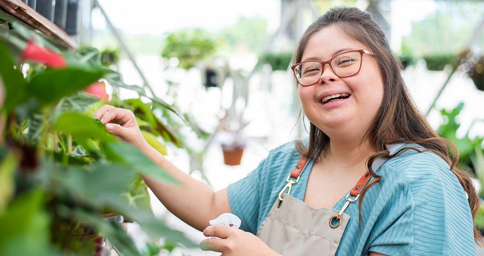 A woman with down syndrome working in a gardening greenhouse and smiling.