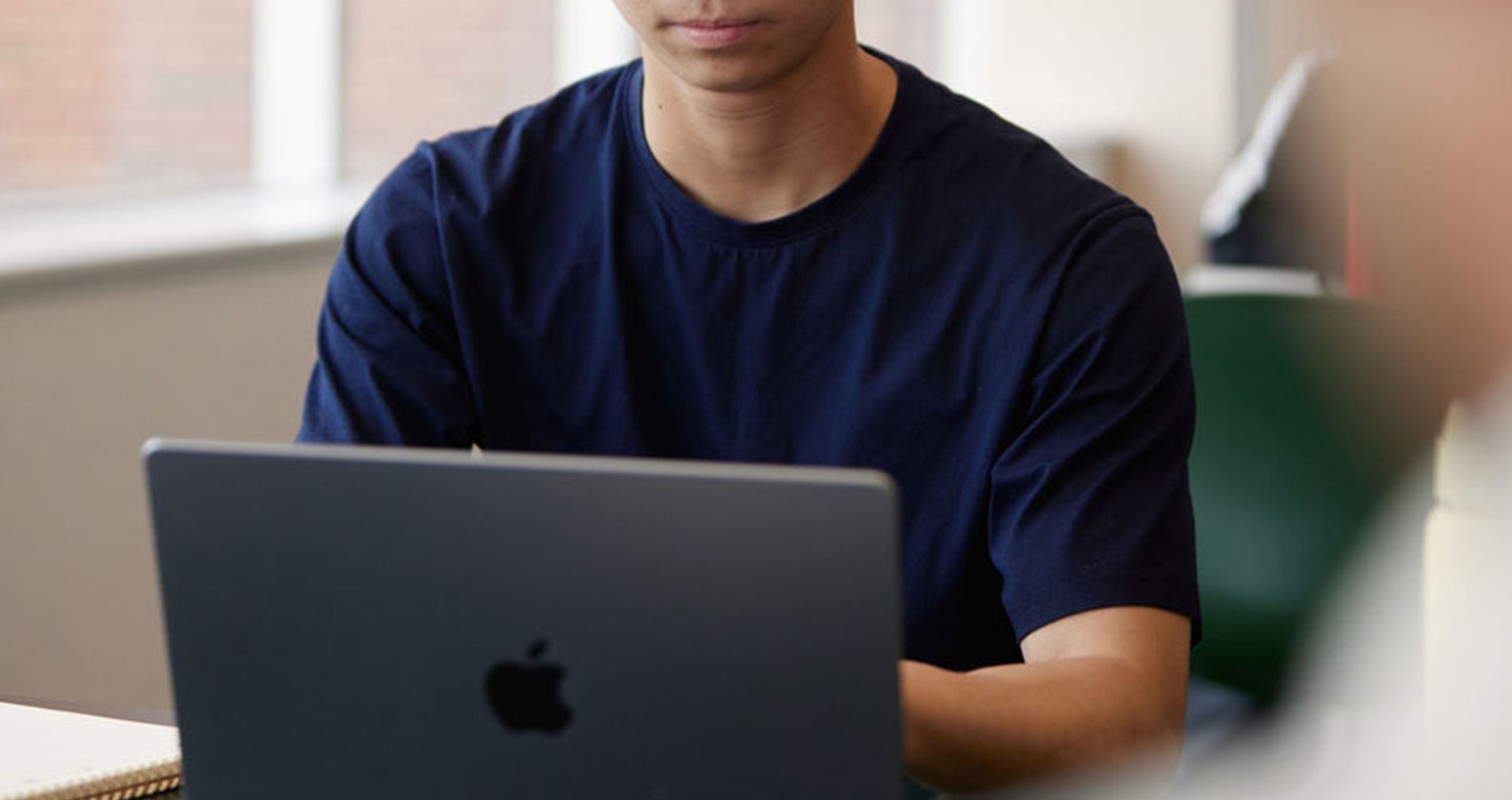 A male student typing on an Apple MacBook.