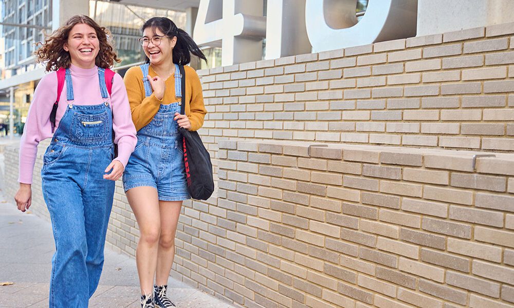 Two girls walking and laughing through campus