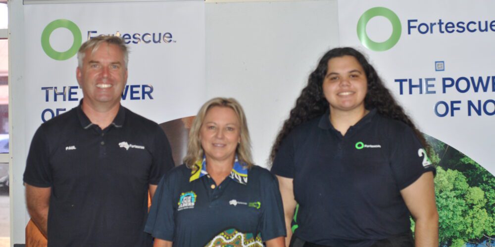 Three Fortescue Metals staff members wearing company polos standing in front of pull up banners.