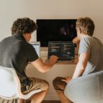Two men use coding software on a laptop.