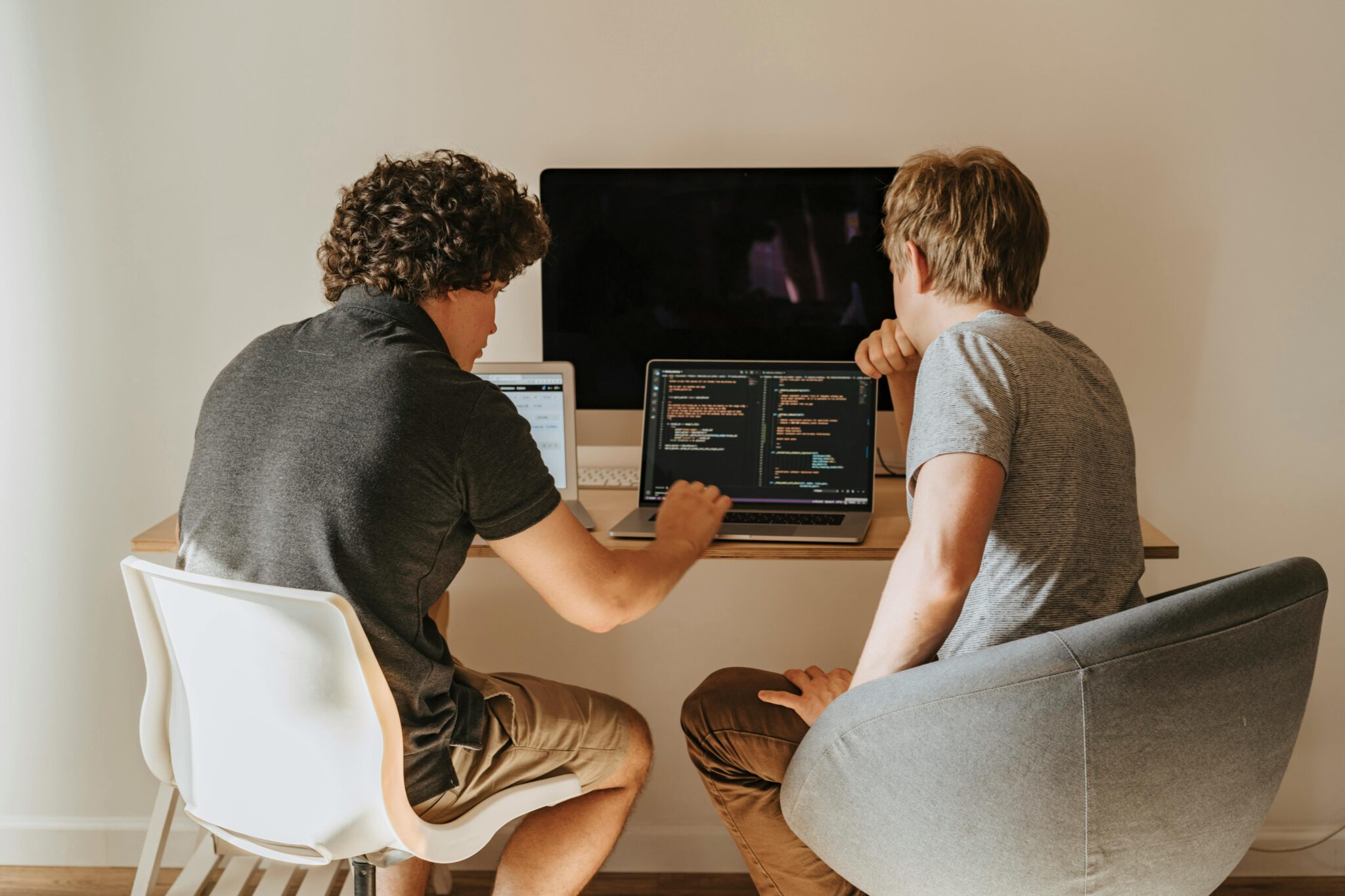 Two men use coding software on a laptop.