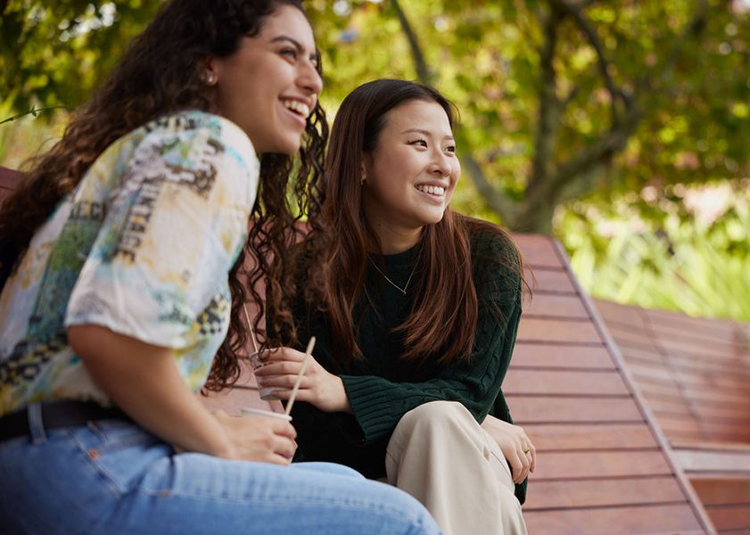two young students laughing on a bench together