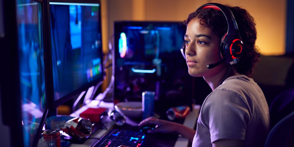 Young woman wearing a headset, gaming using dual computer screens