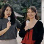 Hosts Devna and Celena stand presenting at the camera, near building 502
