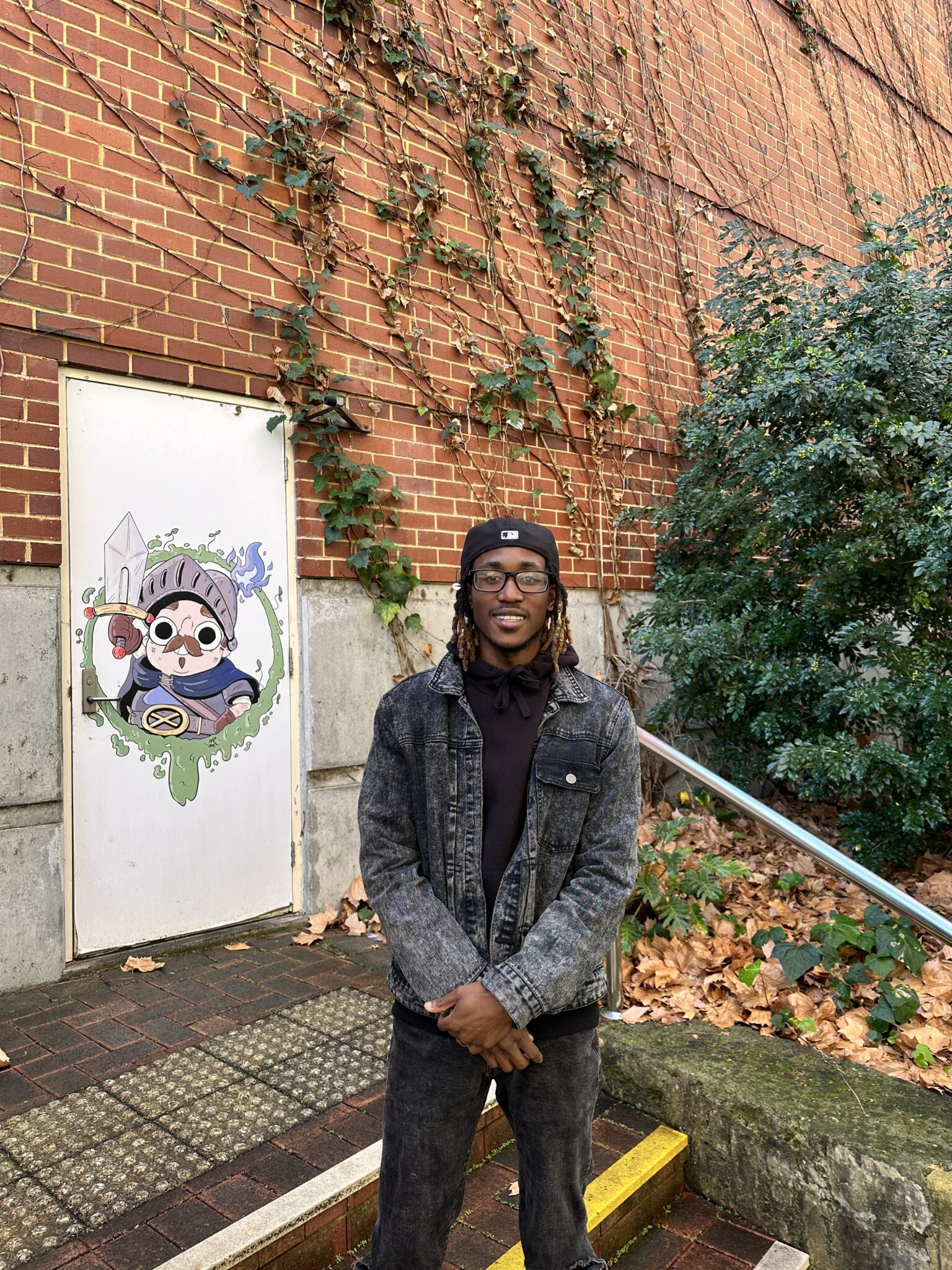 A student, Ortinel, stands smiling in front of some art and greenery.