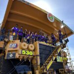 A large mining truck with students posing for a photo at its helm.