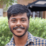 Parashu is smiling in front of some greenery.