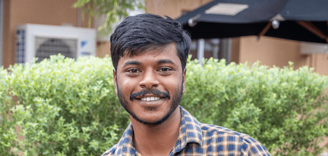 Parashu is smiling in front of some greenery.