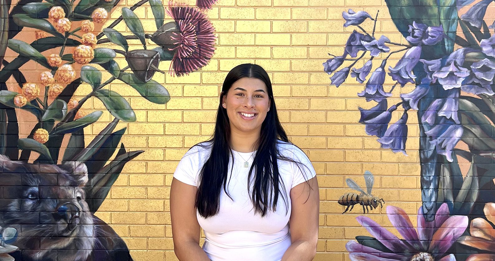 Shayera smiles in front of a Curtin Kalgoorlie mural.