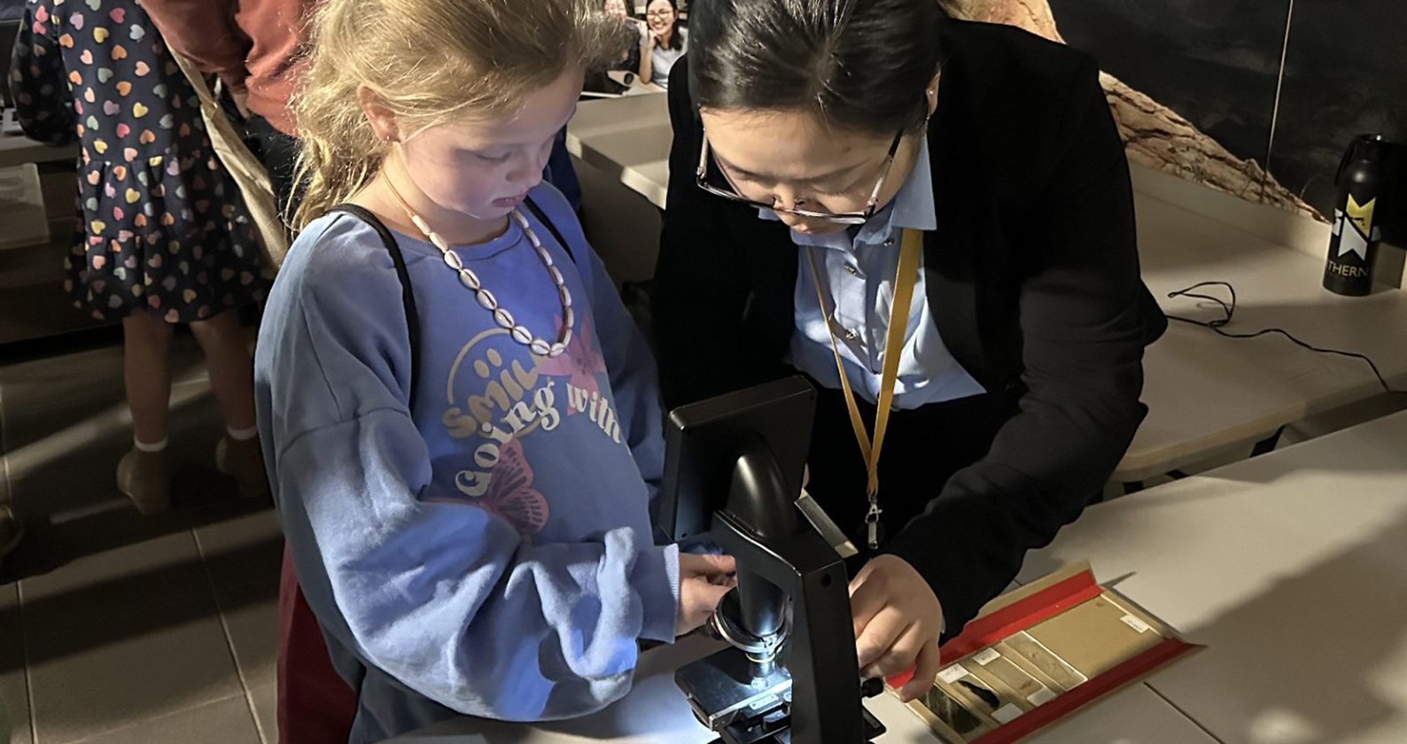 A child and adult use a microscope together.