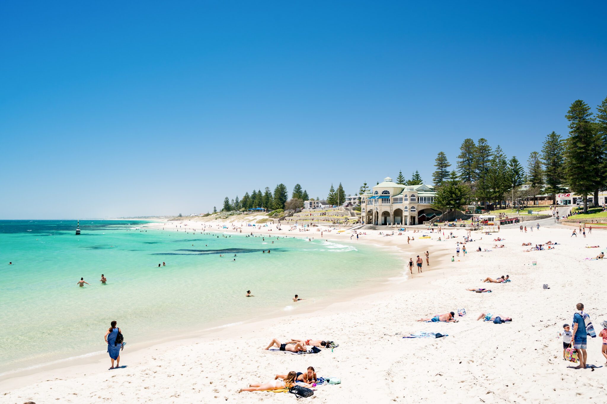 A white sandy beach with aquamarine waters. A white historical building overlooks the ocean.
