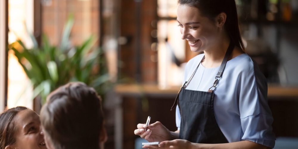 Smiling female waitress takes order or two restaurant visitors.