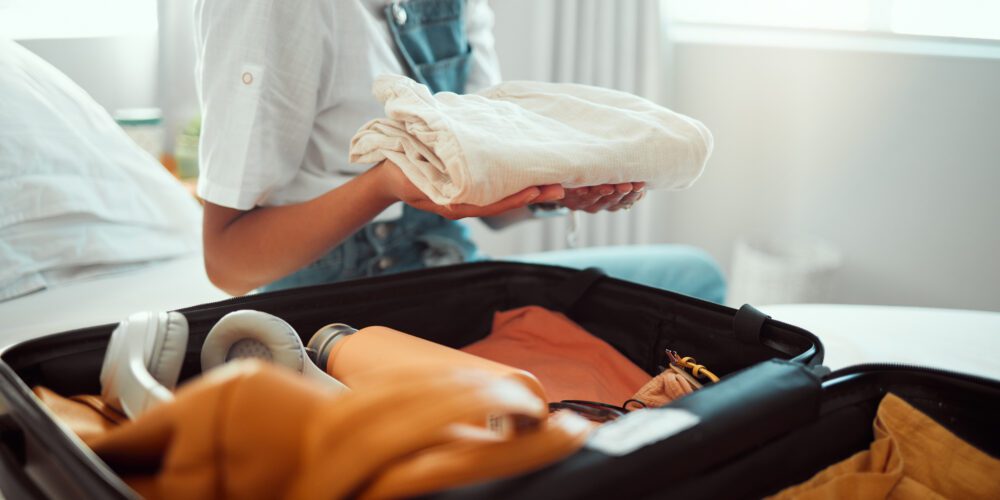 A person sits on a bed packing a suitcase. 