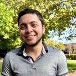 Carlos smiles at the camera with lush campus gardens behind him.